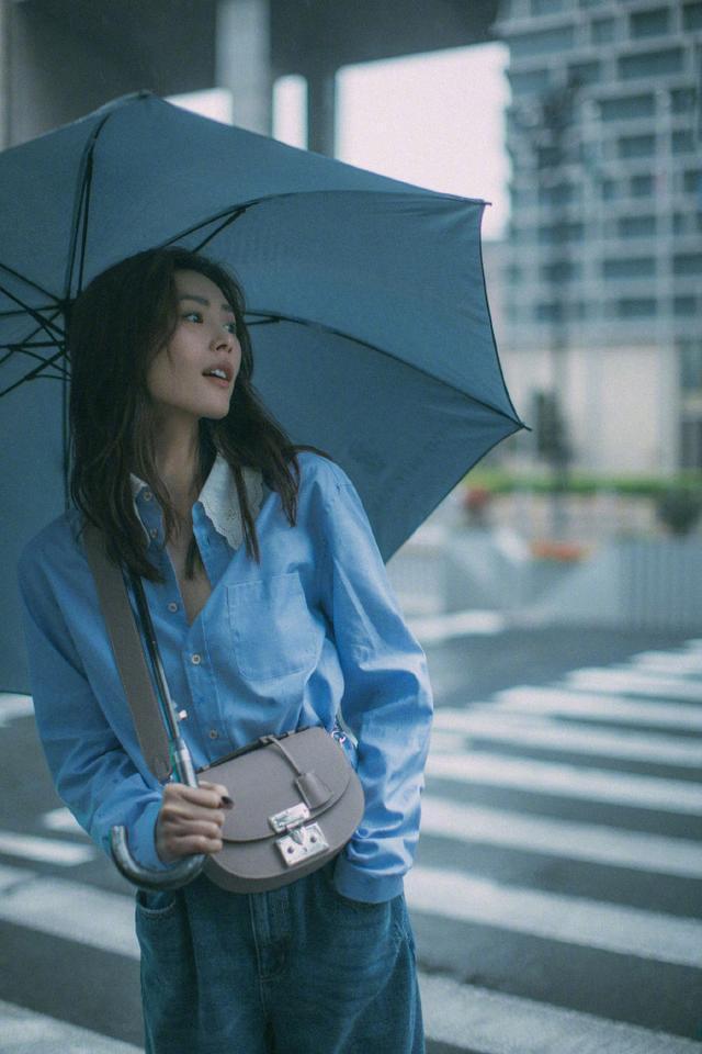 刘雯不愧是超模，雨中撑伞氛围感好强，蓝衬衫配牛仔裤摩登又随性