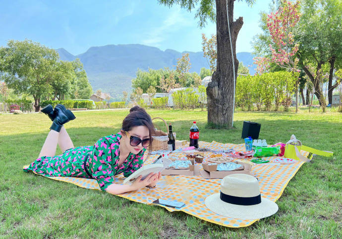 刘亦菲分享出自己户外野餐的照片，身穿绿色清新长裙，戴着墨镜，趴在草地上看书